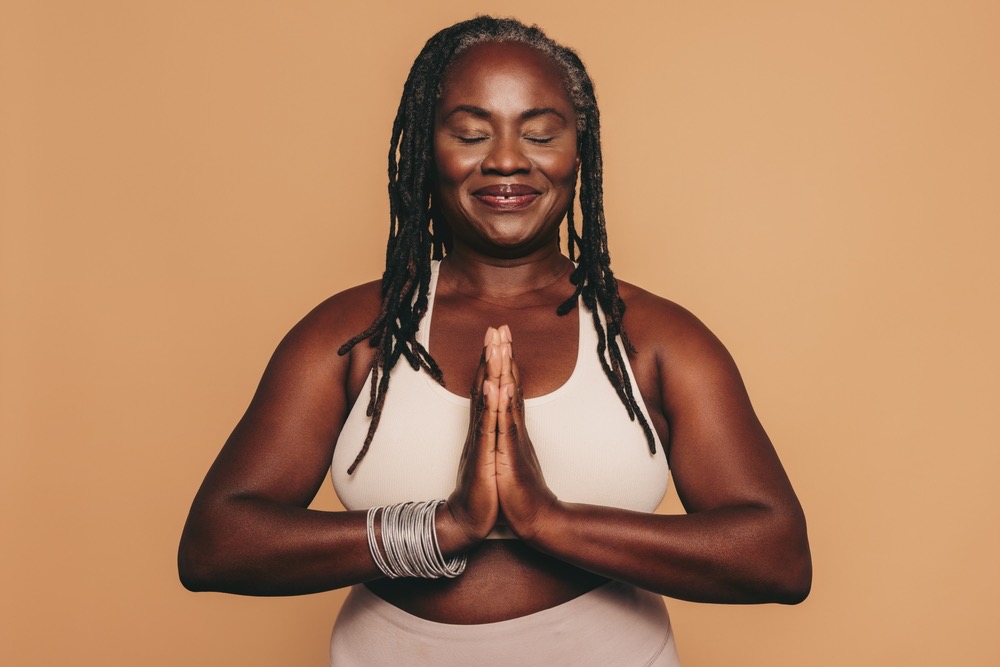 A smiling woman meditating with her hands at her heart