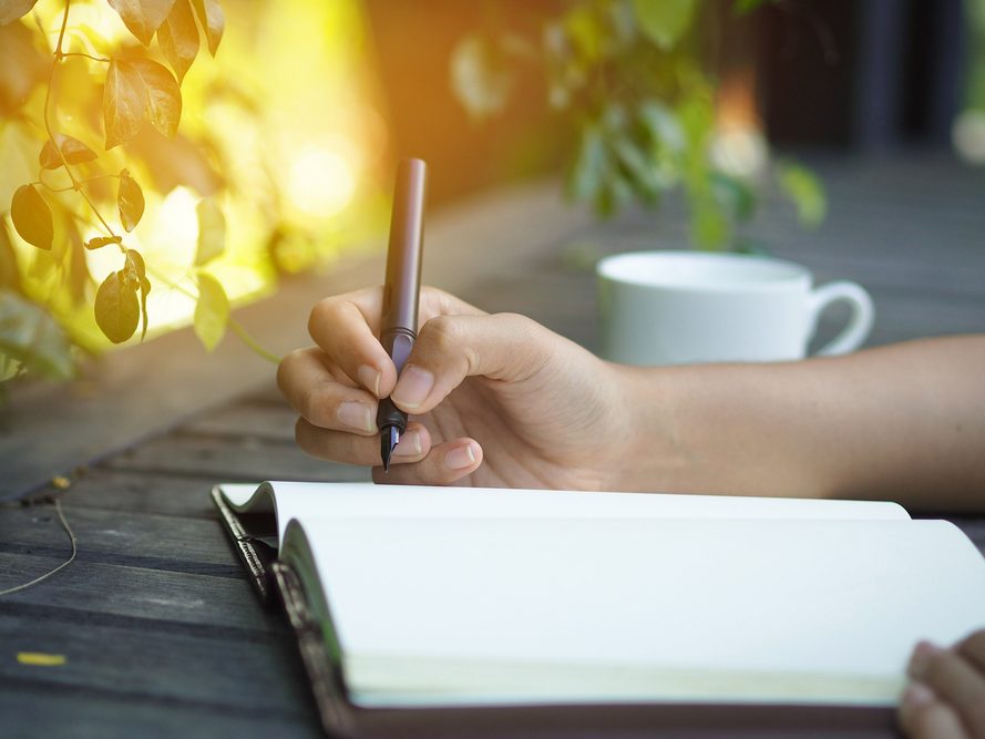 A hand writing in a journal in warm light